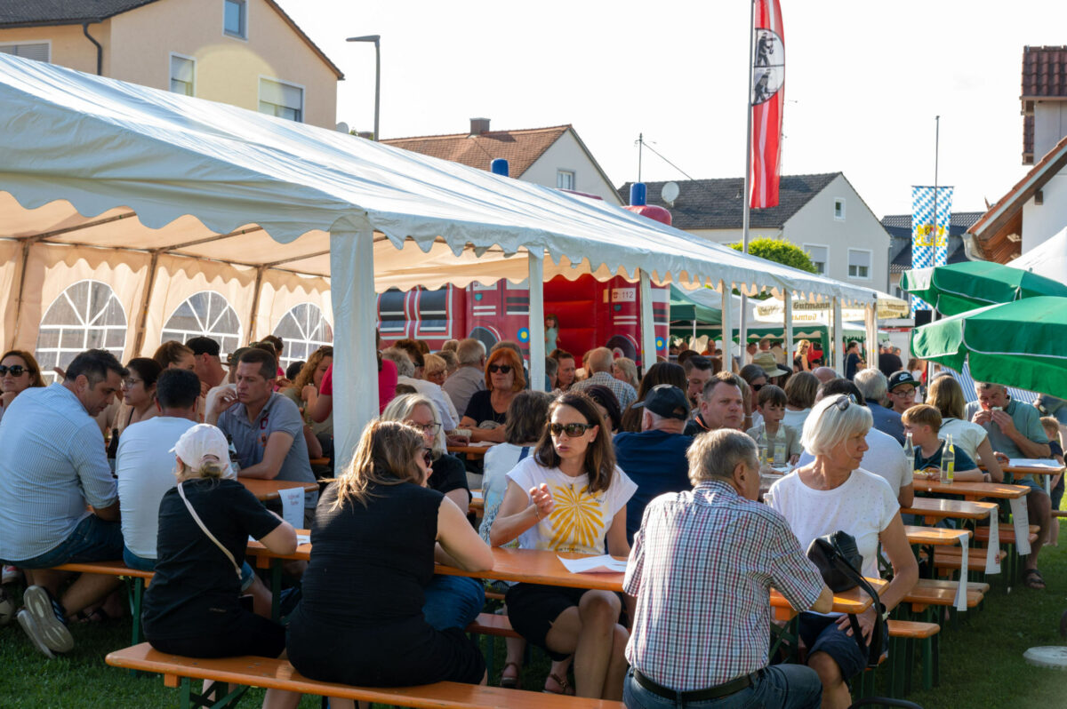 Viele Personen sitzen auf Bierbänken unter einem Zelt. Im Hintergrund eine Hüpfburg.